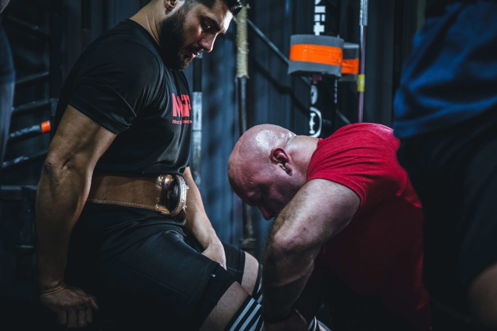 Man helping second man put on a weightlifting belt